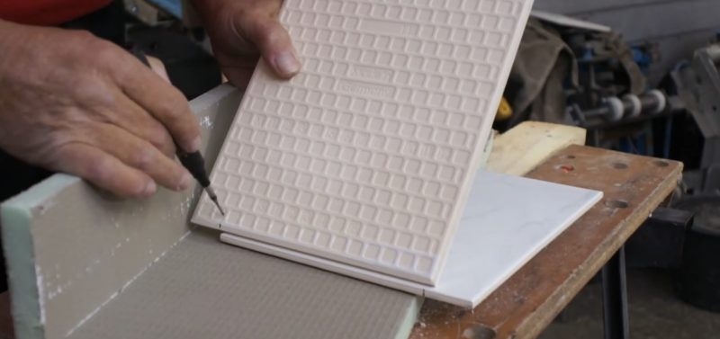 Die Fliese, die zugeschnitten werden soll haltest du parallel zur bereits eingelegten Fliese und zeichnest das kurze Ende mit einem Bleistift an. Die Fliese, die zugeschnitten werden soll haltest du parallel zur bereits eingelegten Fliese und zeichnest das kurze Ende mit einem Bleistift an.